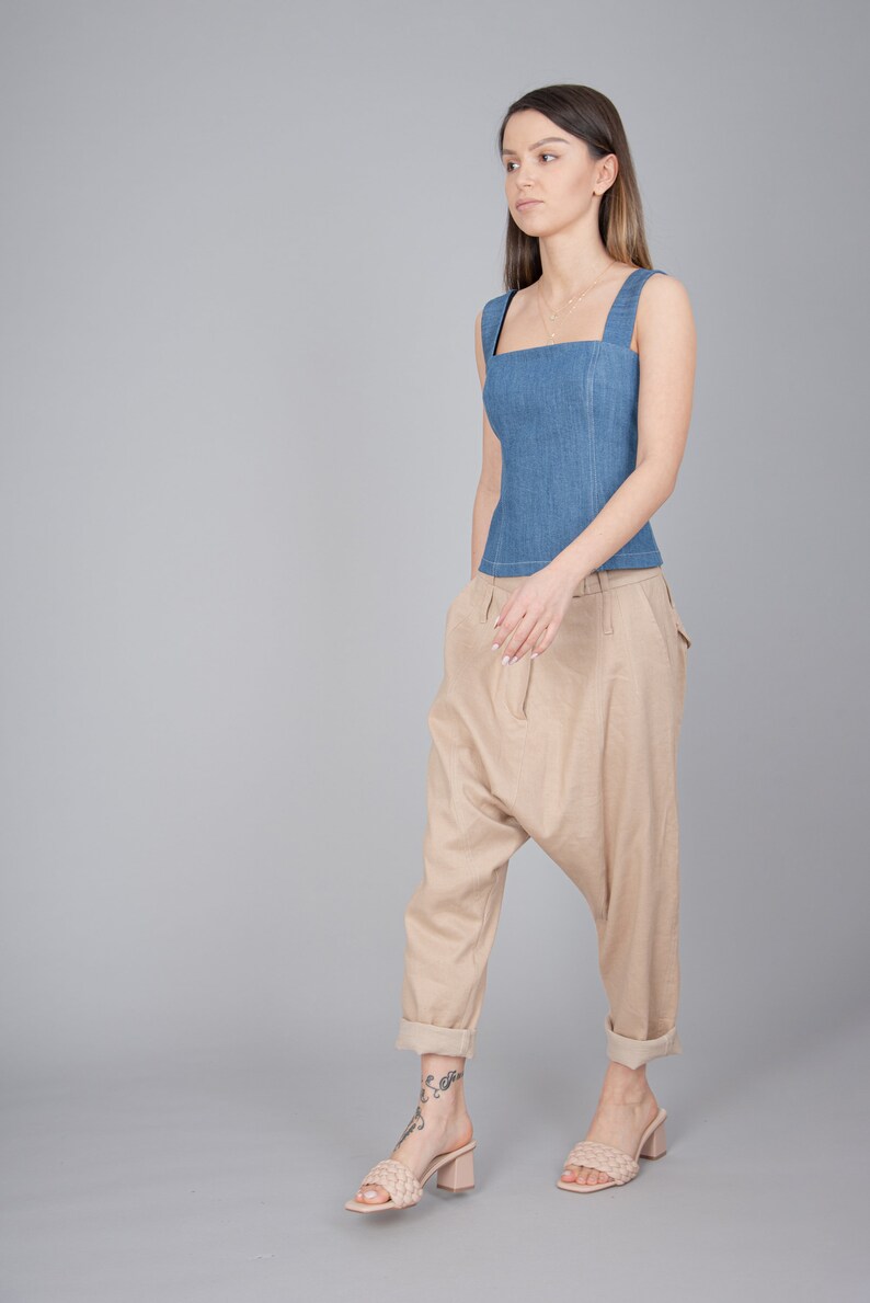 May include: A woman wearing a blue denim sleeveless top and beige, loose-fitting trousers. She is wearing light brown heeled sandals.