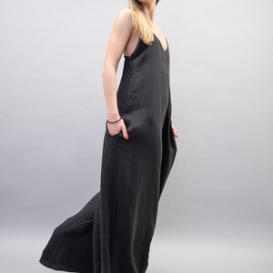 May include: A woman wearing a black, sleeveless jumpsuit with a wide leg. The jumpsuit has a V-neckline and is made of a soft, flowing fabric.