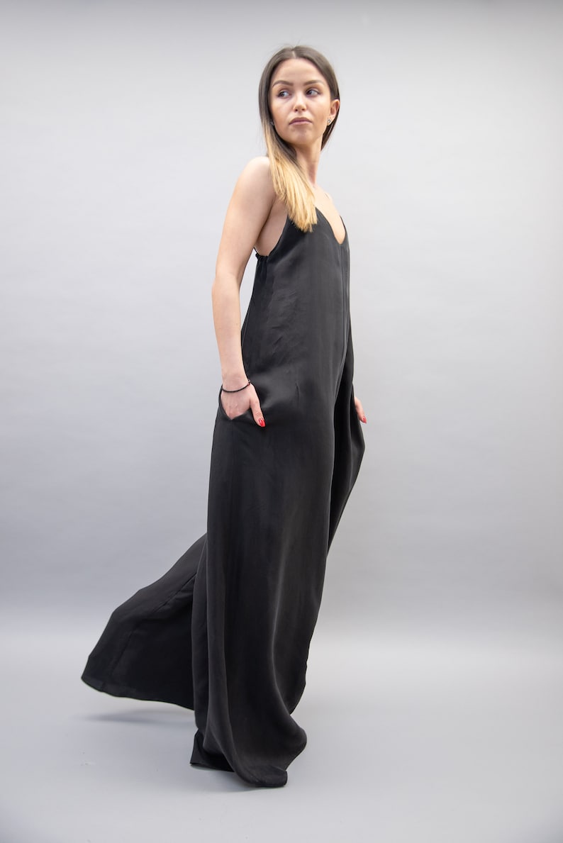 May include: A woman wearing a black, sleeveless jumpsuit with a wide leg. The jumpsuit has a V-neckline and is made of a soft, flowing fabric.