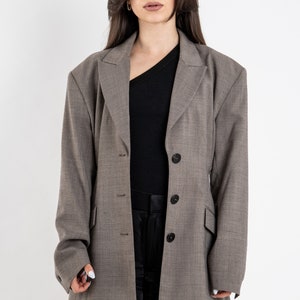 May include: A gray blazer with a single button closure and a slightly oversized fit. The blazer has a textured fabric and a classic lapel.