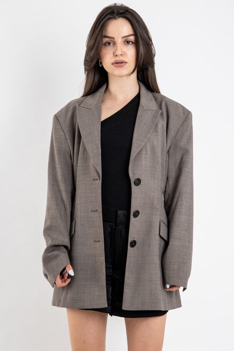 May include: A gray blazer with a single button closure and a slightly oversized fit. The blazer has a textured fabric and a classic lapel.