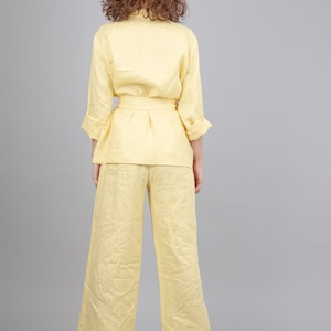 May include: A yellow linen pantsuit with a matching top and trousers. The top has a long sleeve and a belt. The trousers are wide-legged.