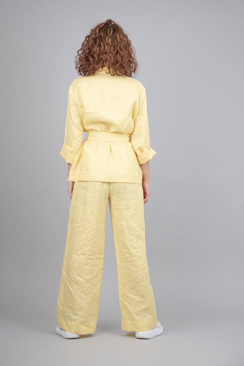May include: A yellow linen pantsuit with a matching top and trousers. The top has a long sleeve and a belt. The trousers are wide-legged.