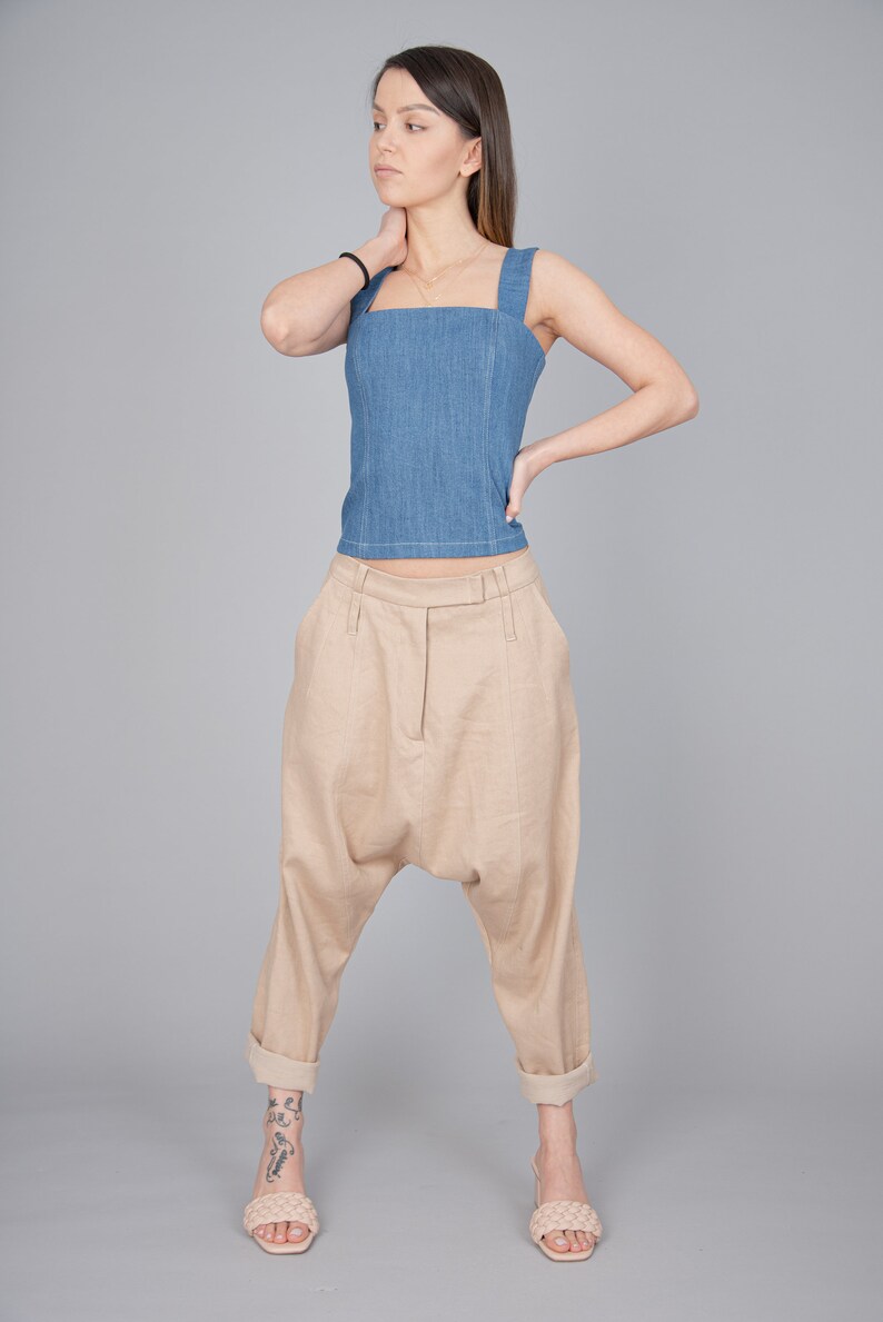 May include: A woman wearing a light blue denim tank top and beige linen trousers with a loose, wide-leg fit. She is wearing light beige sandals.