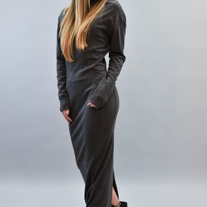 May include: A long, dark gray dress with long sleeves and a high neckline. The dress features a side slit and is paired with black high-heeled ankle boots. The model has long, blonde hair.