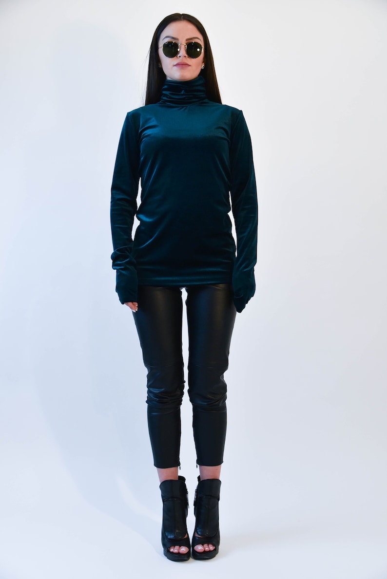 May include: A woman wearing a teal velvet turtleneck sweater and black pants with black heeled boots.
