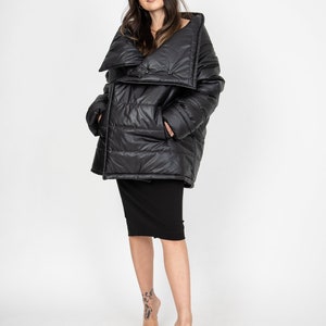 May include: A black puffer jacket with a large, folded collar and a button closure. The jacket has a quilted design and is worn over a black skirt.