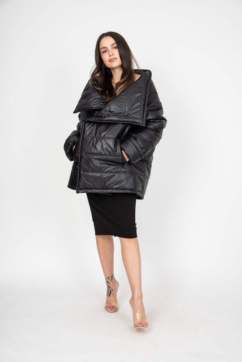 May include: A black puffer jacket with a large, folded collar and a button closure. The jacket has a quilted design and is worn over a black skirt.