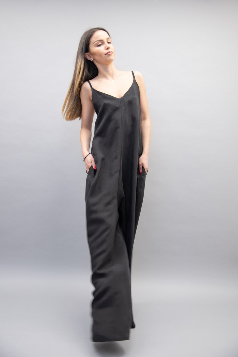 May include: A woman wearing a black sleeveless jumpsuit with a V-neckline. The jumpsuit has a relaxed fit and wide legs.