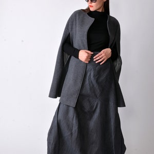 May include: A gray cape with a black turtleneck and a gray pinstripe skirt. The cape has a zipper closure and a collar.