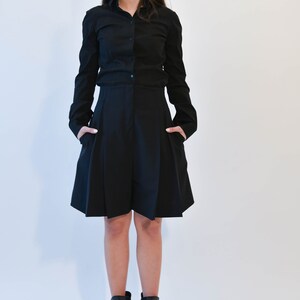 May include: A woman wearing a black button-down shirt and a black pleated skirt. She is wearing black heeled ankle boots with open toes.