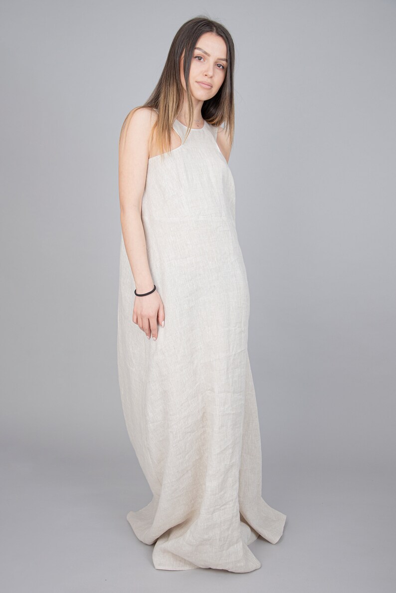 May include: A woman wearing a long, flowing, light beige linen dress. The dress has a halter neckline and a relaxed fit.