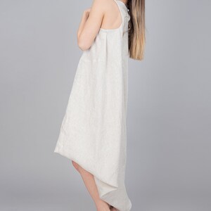 May include: A woman wearing a light beige linen dress with a high neckline and a flowing skirt. She is wearing nude heeled sandals.