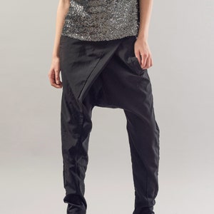 May include: A woman wearing black trousers with a unique design and a silver sequined top.