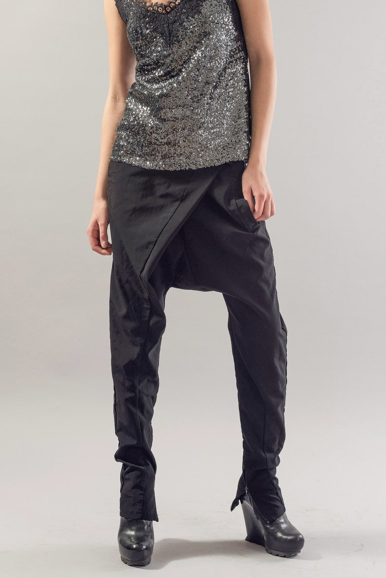 May include: A woman wearing black trousers with a unique design and a silver sequined top.