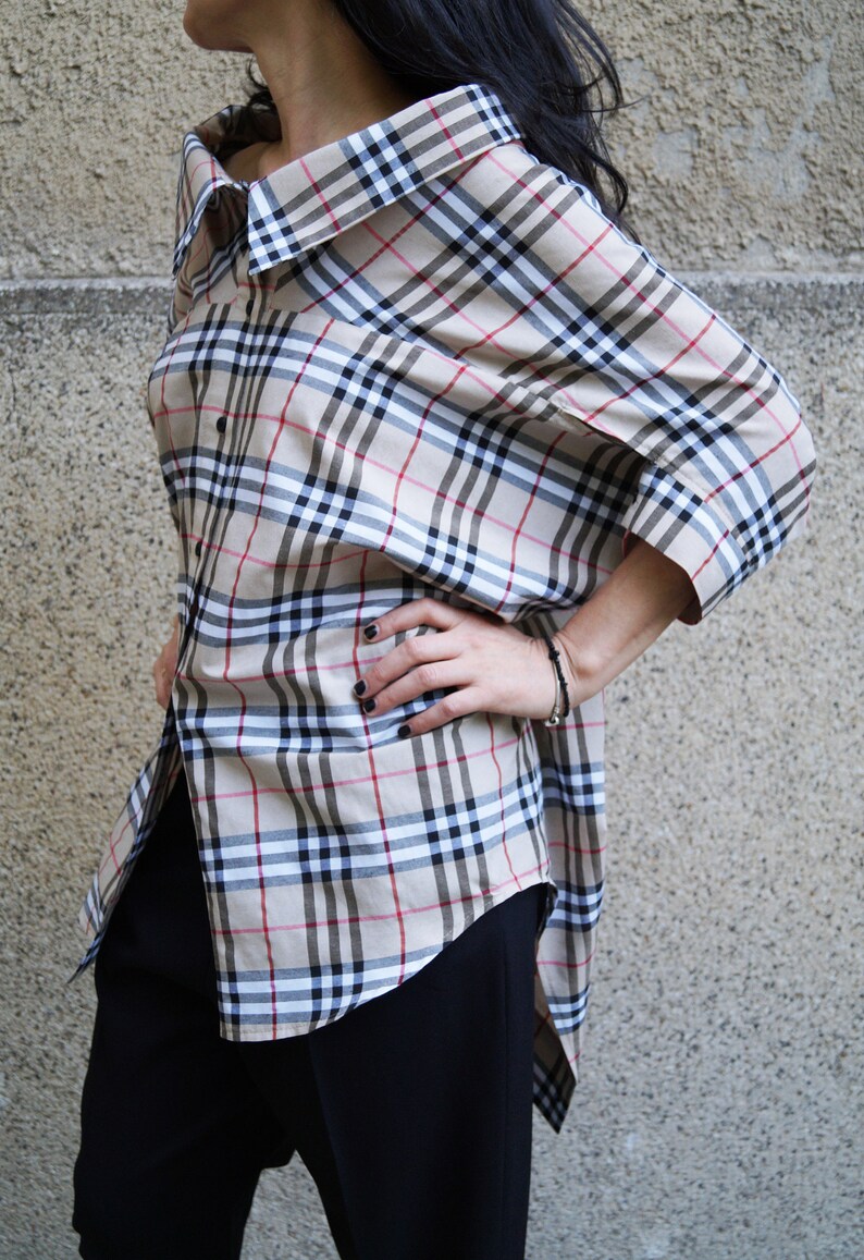 May include: A beige and black checked shirt with a long, asymmetrical hemline. The shirt has a relaxed fit and a collar.
