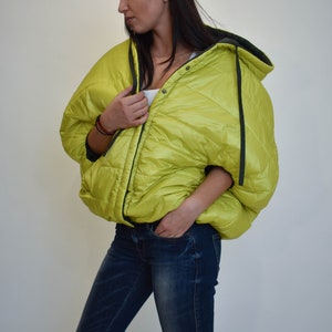 May include: A lime green puffer jacket with a black hood and black trim. The jacket has a zipper closure and a button closure.