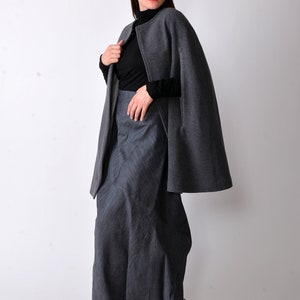May include: A gray cape with a black turtleneck and a long gray skirt. The cape has a zipper closure and a slit on each side. The woman is wearing sunglasses.