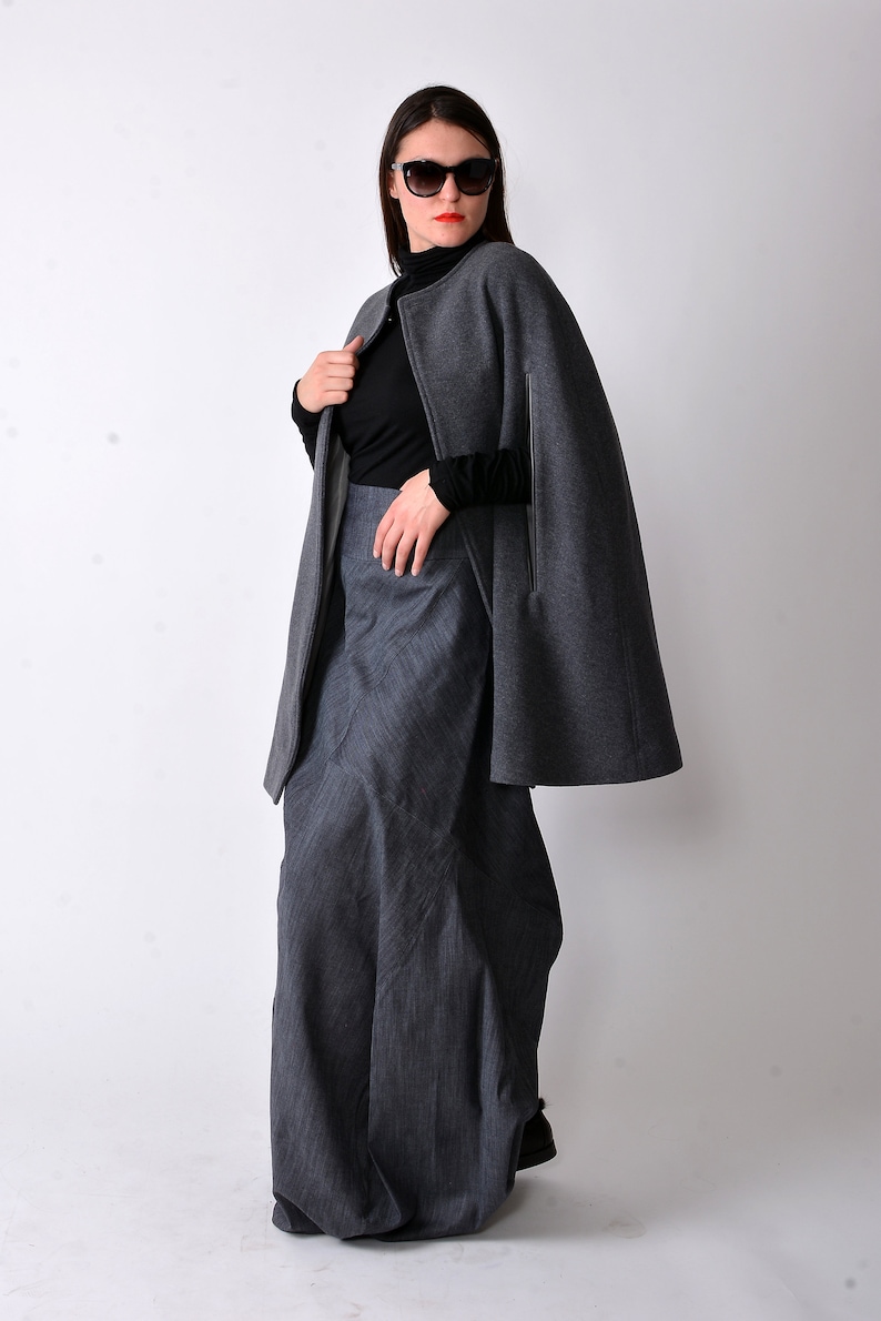 May include: A gray cape with a black turtleneck and a long gray skirt. The cape has a zipper closure and a slit on each side. The woman is wearing sunglasses.