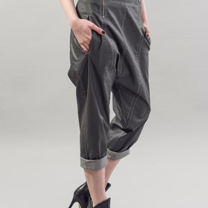 May include: Gray cropped pants with a unique design and a zipper detail. The pants have a cuffed hem and are styled with black heeled ankle boots.