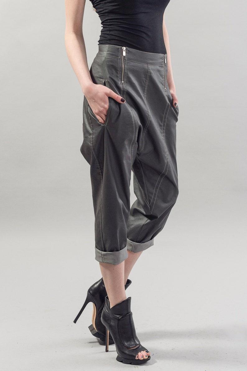 May include: Gray cropped pants with a unique design and a zipper detail. The pants have a cuffed hem and are styled with black heeled ankle boots.