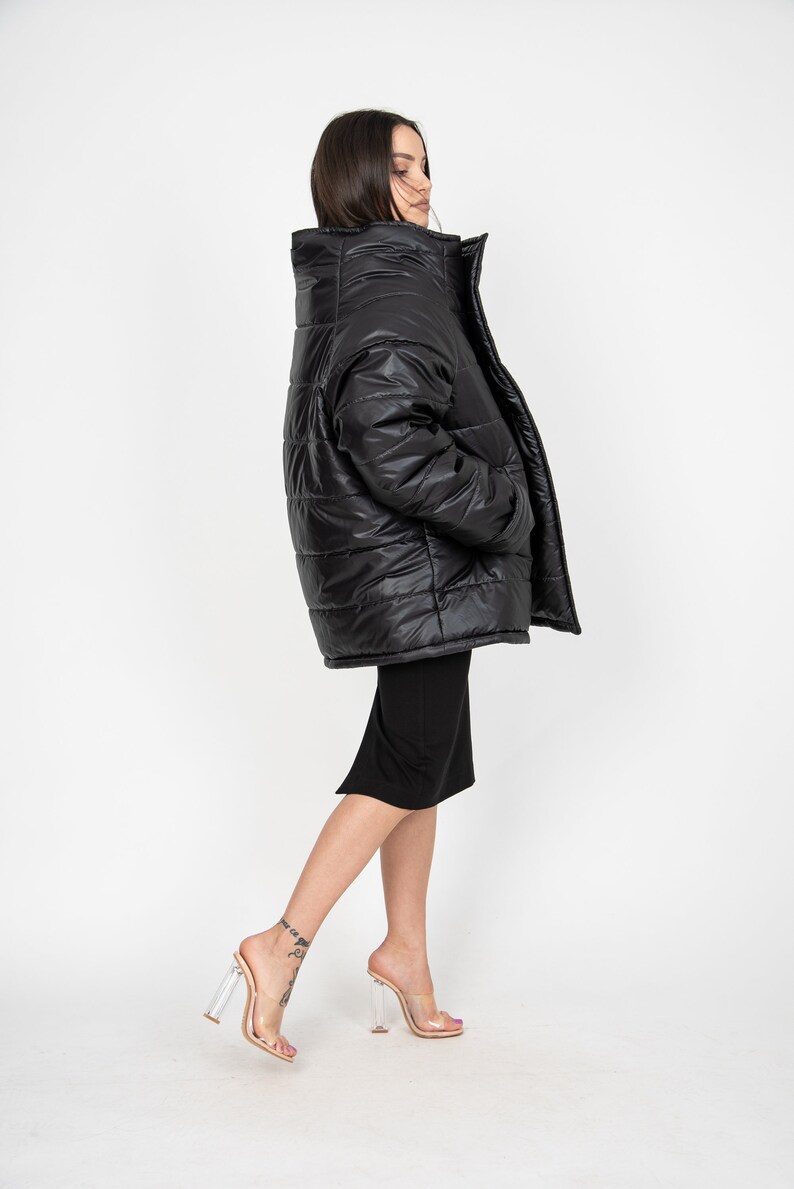 May include: A black puffer jacket with a high collar and a zipper closure. The jacket is worn by a person with long dark hair and is standing on a white background.