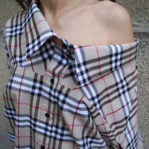 May include: A beige and black checked shirt with a loose fit and a collar that is folded down. The shirt is made of a soft, lightweight fabric and has a casual, relaxed style.