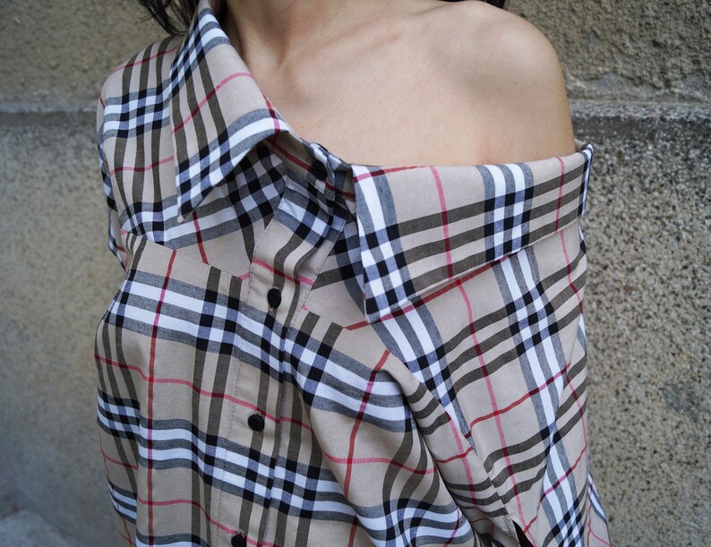 May include: A beige and black checked shirt with a loose fit and a collar that is folded down. The shirt is made of a soft, lightweight fabric and has a casual, relaxed style.