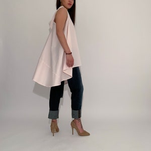 May include: A woman wearing a light pink sleeveless top with a high-low hemline and blue jeans. She is wearing brown high heels.
