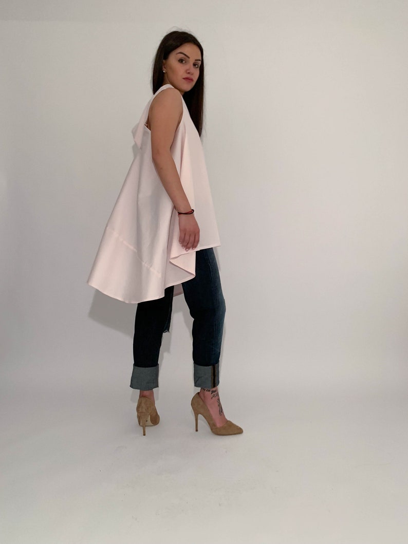 May include: A woman wearing a light pink sleeveless top with a high-low hemline and blue jeans. She is wearing brown high heels.