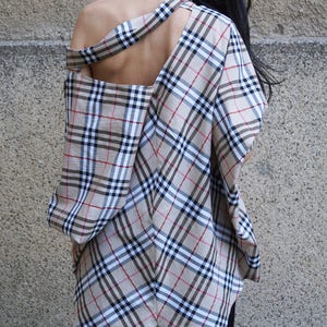 May include: A plaid shirt with a cut-out back and a long, asymmetrical hemline. The shirt is made of a lightweight fabric and has a relaxed fit.