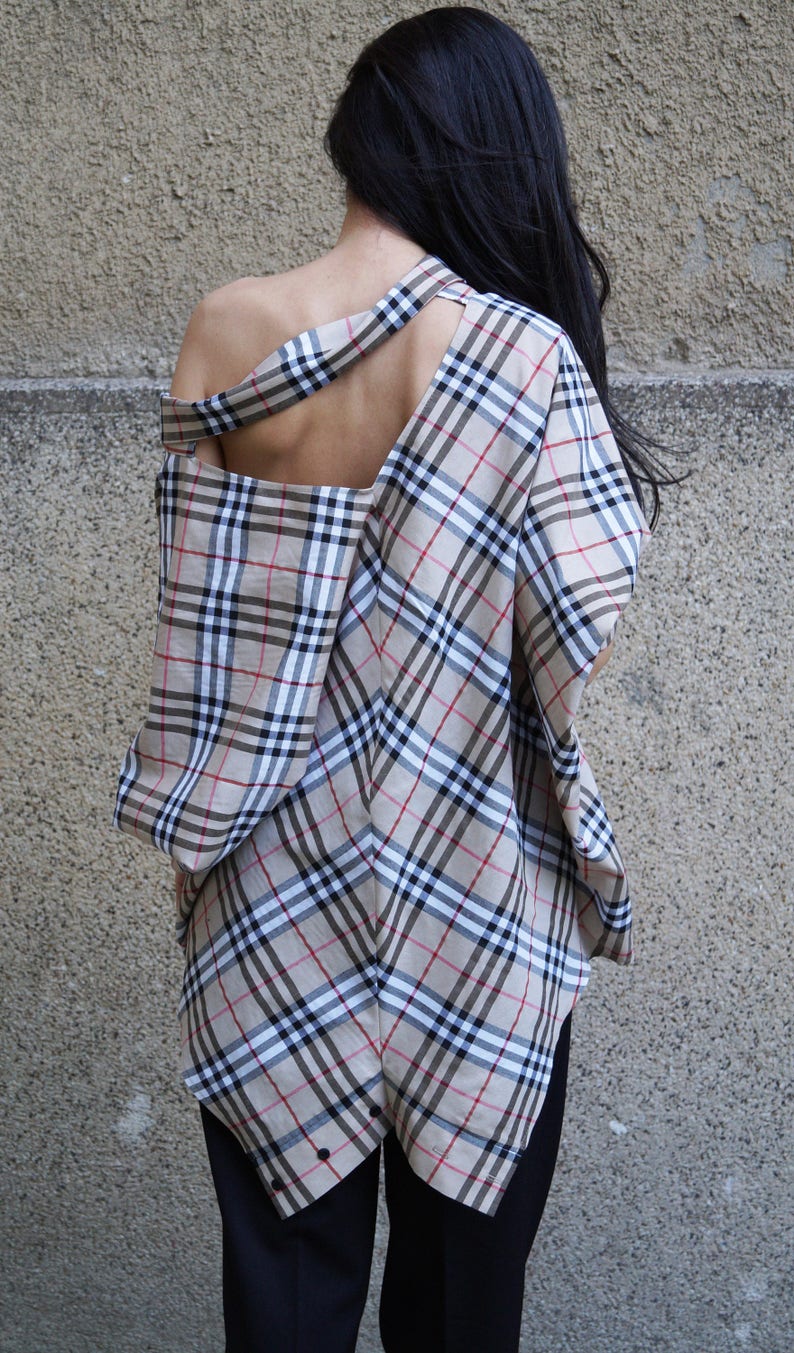 May include: A plaid shirt with a cut-out back and a long, asymmetrical hemline. The shirt is made of a lightweight fabric and has a relaxed fit.