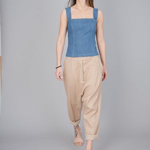 May include: A woman wearing a light blue denim sleeveless top and beige wide-leg trousers. She is wearing beige sandals and has a gold necklace.