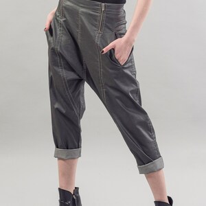 May include: Gray cropped pants with a cuffed hem and a zipper detail. The pants are made of a shiny fabric and have a loose fit. The model is wearing black heeled shoes.