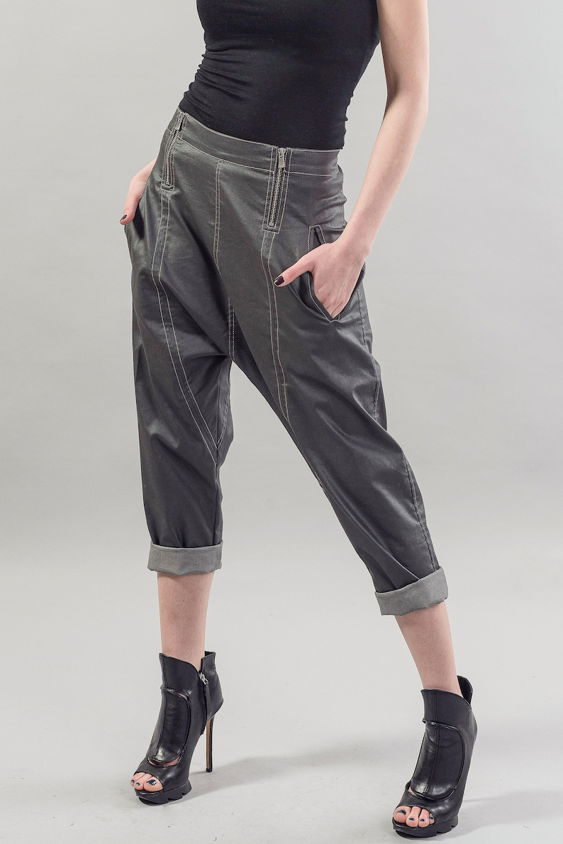 May include: Gray cropped pants with a cuffed hem and a zipper detail. The pants are made of a shiny fabric and have a loose fit. The model is wearing black heeled shoes.