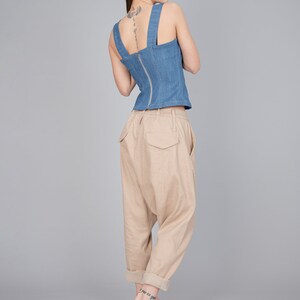 May include: A woman wearing a blue denim corset top with a zip down the back and beige, loose-fitting trousers. She is wearing beige heeled sandals with a woven strap.