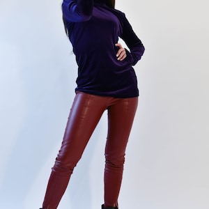 May include: A woman wearing a purple velvet turtleneck top and burgundy leather pants. She is wearing black heeled boots and sunglasses.