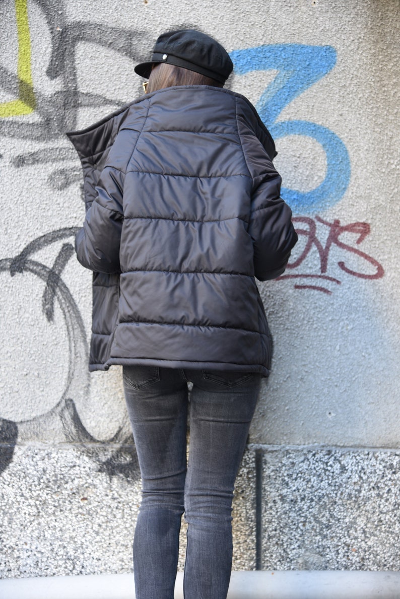May include: A black puffer jacket with a high collar and a zipper closure. The jacket is worn over a pair of dark wash jeans.