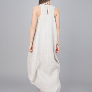 May include: A beige linen dress with a loose, flowing silhouette. The dress has a sleeveless design and a scoop neckline.