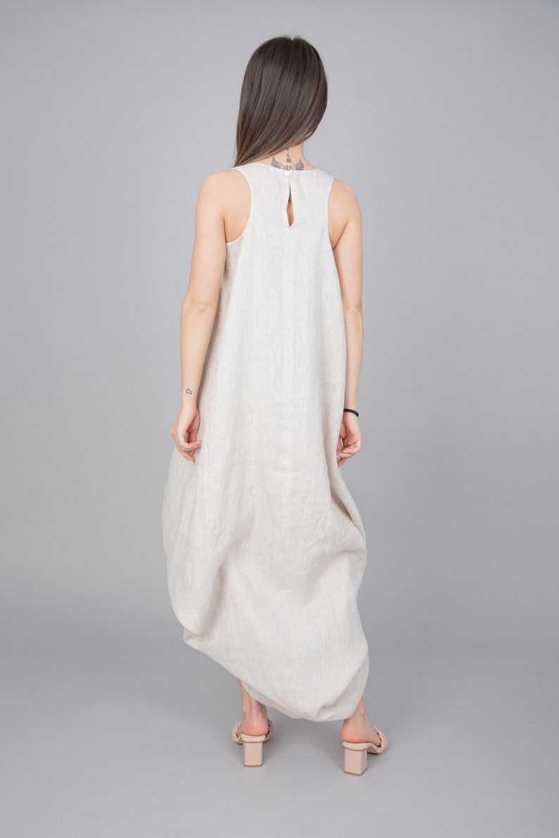 May include: A beige linen dress with a loose, flowing silhouette. The dress has a sleeveless design and a scoop neckline.