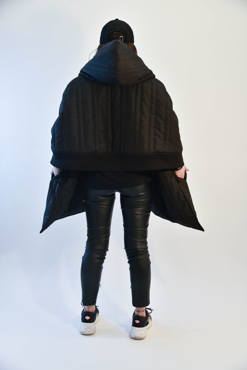 May include: A black quilted hooded jacket with a zipper closure and a black baseball cap with the word "SQUARED" on the front. The jacket is worn over black pants and black sneakers.