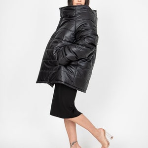 May include: A black puffer jacket with a high collar and a quilted design. The jacket is oversized and has a relaxed fit. The model is wearing the jacket with a black skirt and clear heeled sandals.