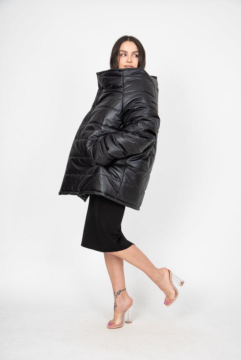 May include: A black puffer jacket with a high collar and a quilted design. The jacket is oversized and has a relaxed fit. The model is wearing the jacket with a black skirt and clear heeled sandals.