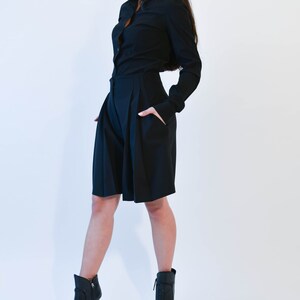 May include: A woman wearing a black long-sleeved shirt and black shorts. She is wearing black heeled ankle boots with open toes.
