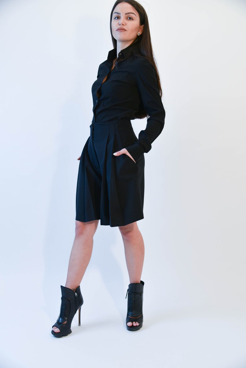 May include: A woman wearing a black long-sleeved shirt and black shorts. She is wearing black heeled ankle boots with open toes.