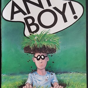 Può includere: Una copertina di fumetto con sfondo verde e un fumetto bianco che dice "ANT BOY!" in lettere nere. Un personaggio dei cartoni animati con un pezzo di terra e erba sulla testa spunta da un buco nel terreno. Il personaggio indossa una camicia blu e ha grandi occhiali neri.