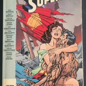 May include: Comic book cover titled "The Death of Superman." The artwork shows a woman weeping as she holds Superman, who is injured. The background features a ruined city and a damaged Superman logo.