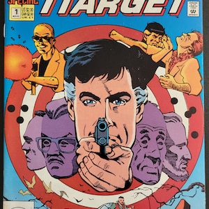 May include: The Human Target comic book cover, featuring a man holding a gun with a target behind him. The cover is red, white, and blue with the title "The Human Target" in large, bold letters. The comic book is issue number 1 and is published by DC Comics.