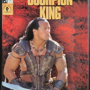 Puede incluir: La portada del cómic The Scorpion King presenta un primer plano de Dwayne Johnson como el personaje principal, sosteniendo una espada. Lleva una armadura de cuero y un collar. El fondo es de color rojo y naranja.