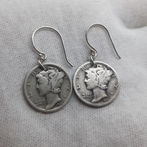 May include: A pair of silver earrings featuring a 1926 Walking Liberty half dollar coin. The coins are attached to silver hooks.